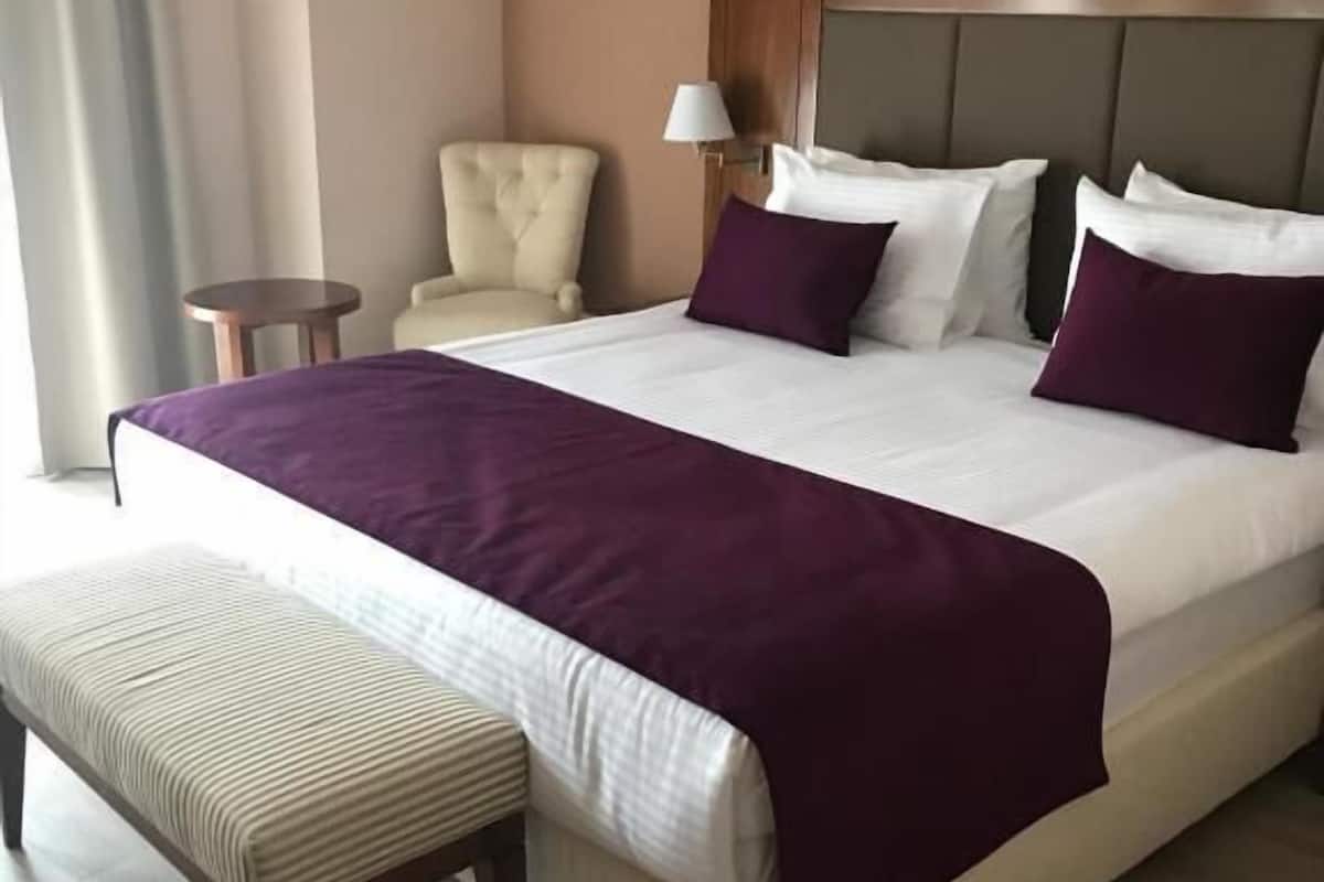 Una habitación de hotel con una cama grande, una mesita de noche, una silla y un banco.