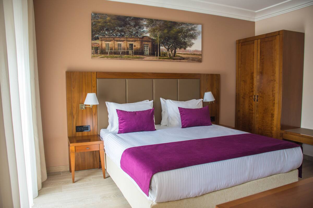 Un dormitorio con una cama grande, dos mesitas de noche, un armario de madera y un cuadro en la pared.
