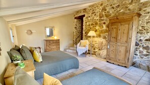 Een slaapkamer met twee bedden, een dressoir, een stoel en een stenen muur.