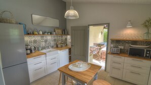 Een kleine keuken met witte kastjes, een houten aanrecht, een spoelbak, een magnetron en een hangende lamp.