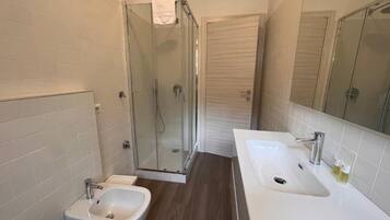 A modern bathroom with a shower, two sinks, and a bidet.