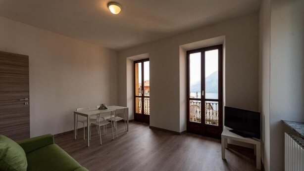 A modern apartment with a dining area, a green sofa, a TV, and large windows with a view. - Regolo House (Perledo)