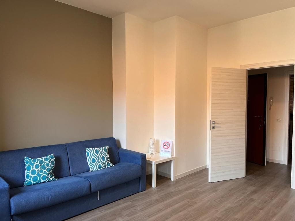 A room with a blue sofa, a small table with a sign, and a door leading to another room.