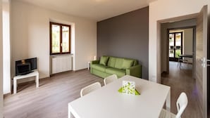A modern living room with a green sofa, a white dining table, and a television on a small stand. - Regolo House (Perledo)