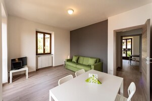A modern living room with a green sofa, a white dining table, and a television on a small stand.