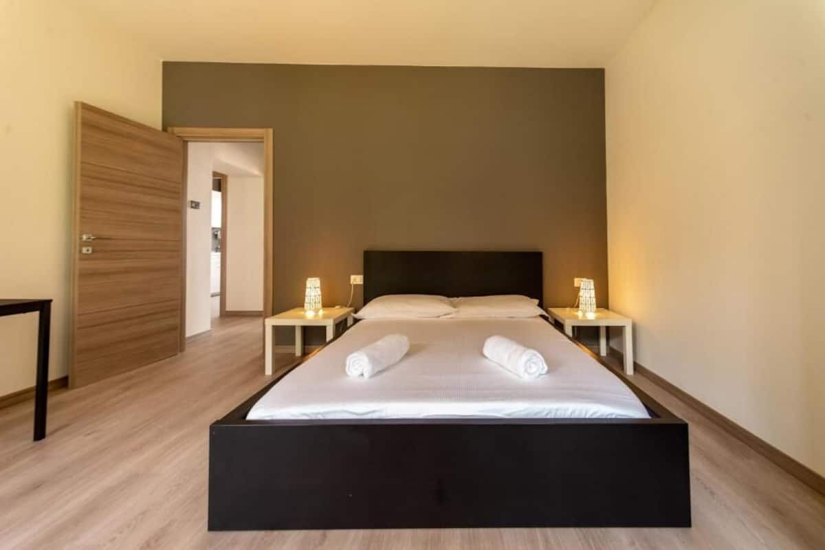 Ein modernes Hotelzimmer mit einem großen Bett, zwei Nachttischen mit Lampen und einer Holztür.