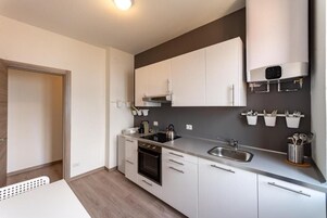 A modern kitchen with white cabinets, a built-in oven, a stainless steel sink, and a wall-mounted heater.