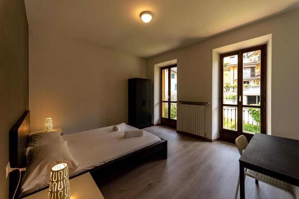 Una camera da letto con un letto, lampade sui comodini, un tavolo e vista su un balcone con ringhiera.