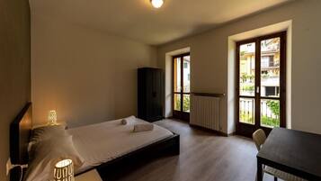 Una camera da letto con un letto, lampade sui comodini, un tavolo e vista su un balcone con ringhiera.