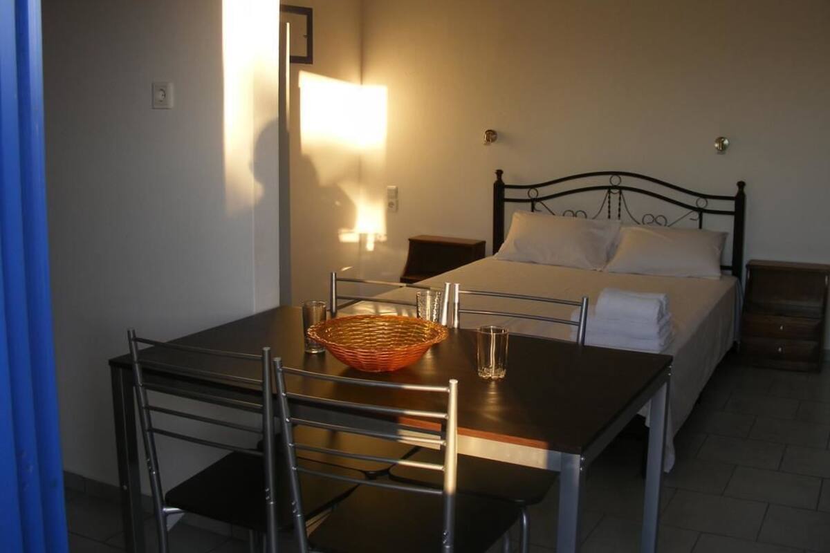A hotel room with a bed, a bedside table, a table with chairs, and a lamp.