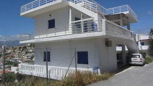 Un edificio de dos pisos con un balcón en el nivel superior, un área cercada y un coche estacionado adelante.