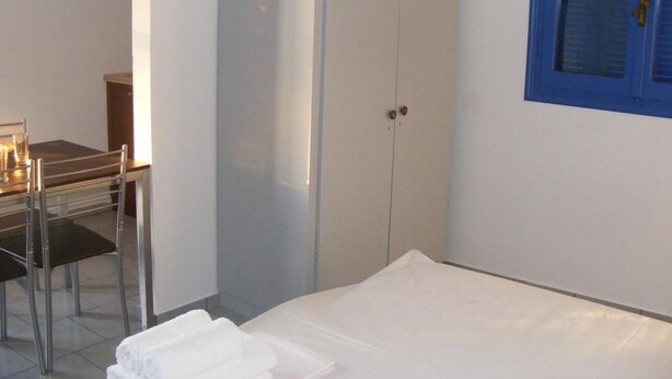 Een slaapkamer met een bed, een kledingkast, een bureau met stoel en een raam met blauwe lijst.