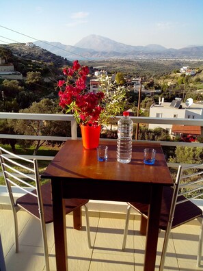A balcony with a table, chairs, a potted plant, and a water bottle. - Panoramakamil (Faistos)