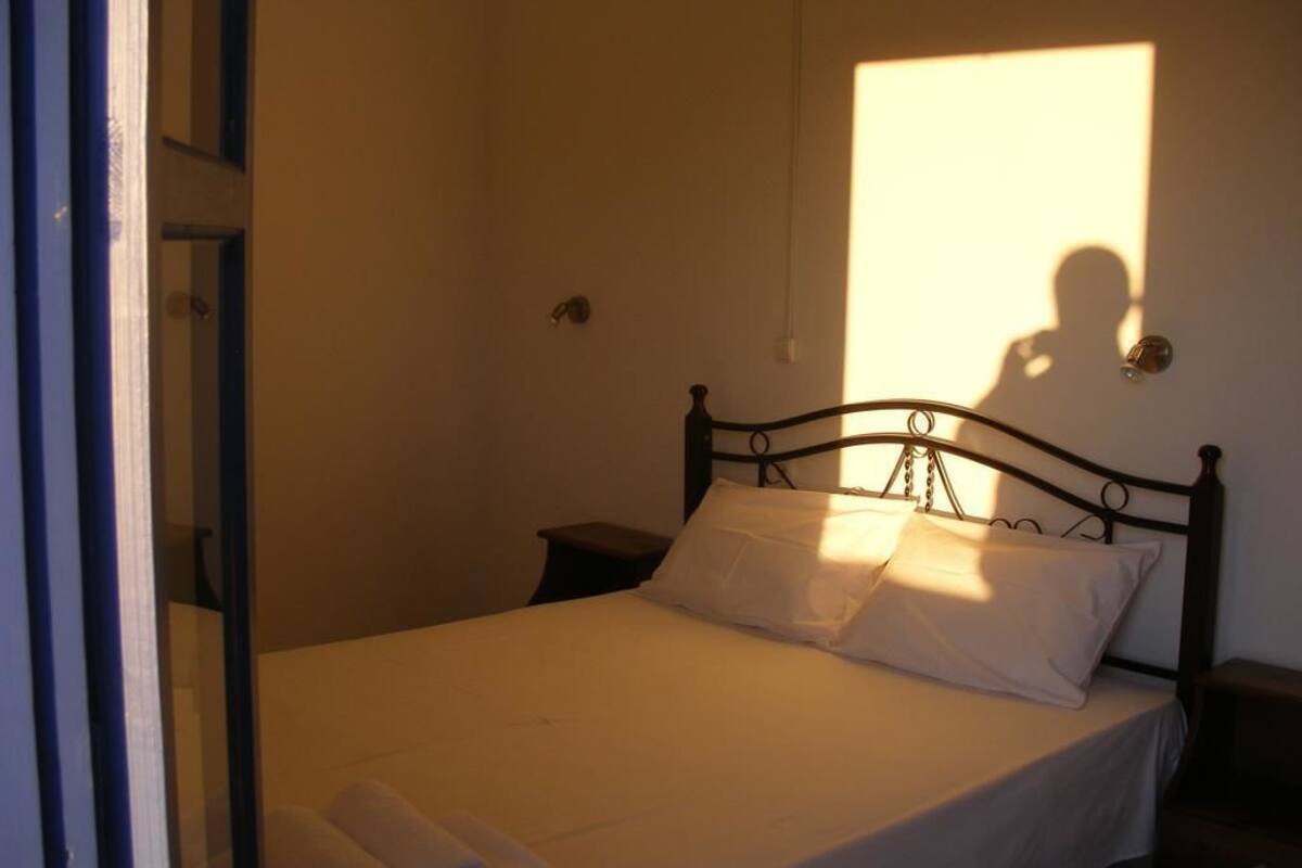A neatly made bed with white linens and pillows, a bedside table, and a wall-mounted light fixture.