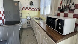 Ett kompakt kök med kylskåp, mikrovågsugn, diskho och ett fönster med gardiner.