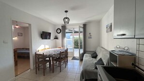 A compact kitchen with a dining table, a sofa, and a TV mounted on the wall. - Cozy Beachside House: Ocean Views, Private Parking, Terrace, BBQ, Pets OK, Free Final Cleaning (Saint-Jean-de-Monts)