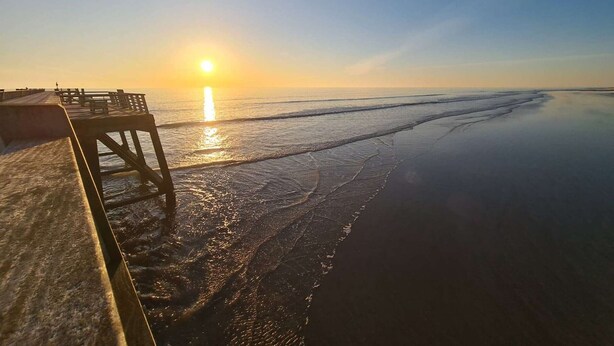 A beach scene with a wooden pier extending into calm waters, a clear sky, and the sun low on the horizon. - Cozy Beachside House: Ocean Views, Private Parking, Terrace, BBQ, Pets OK, Free Final Cleaning (Saint-Jean-de-Monts)