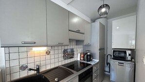 A modern kitchen with grey cabinets, a black sink, a stove, a microwave, and a coffee maker. - Cozy Beachside House: Ocean Views, Private Parking, Terrace, BBQ, Pets OK, Free Final Cleaning (Saint-Jean-de-Monts)