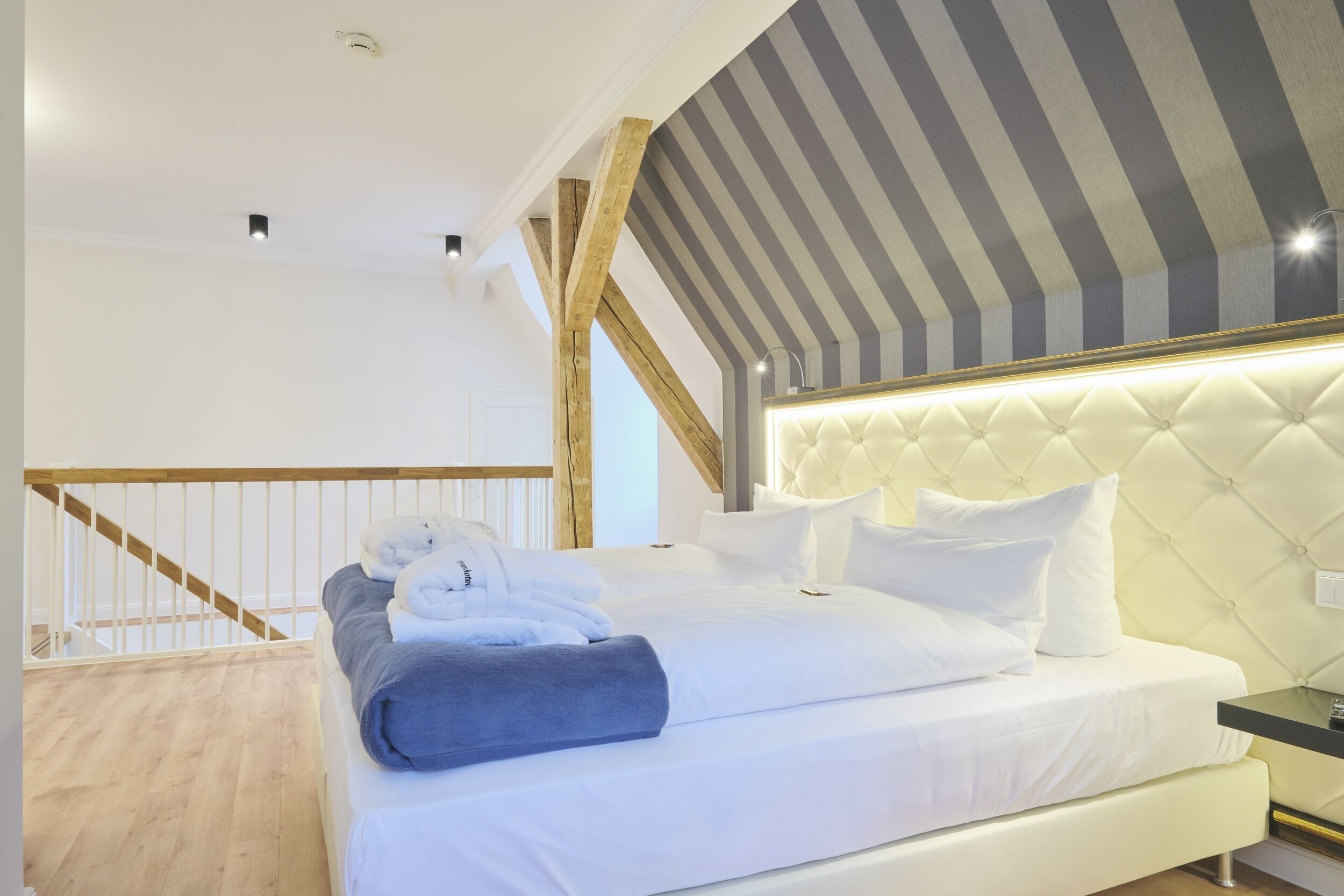 Una habitación de hotel con una cama grande, una escalera de madera y un techo a rayas.