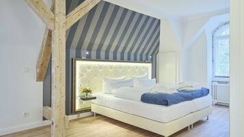 A modern bedroom with a sloped ceiling, a tufted headboard, a white bed, and a view of the outdoors through a window.