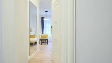 A hallway with a wooden floor, white walls, and a yellow sofa in the background.