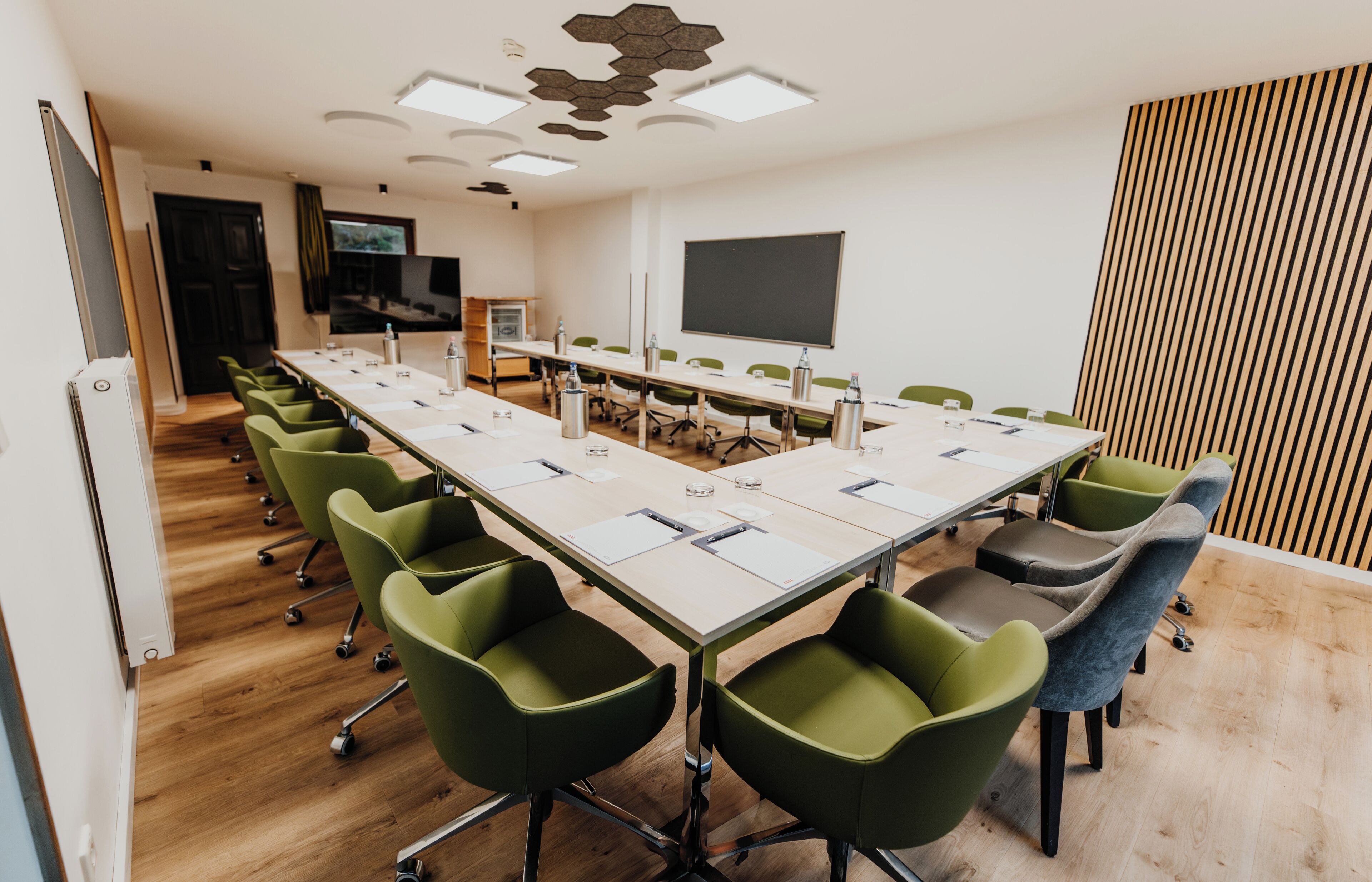 A conference room with a long table, green and gray chairs, a projector, and a blackboard.