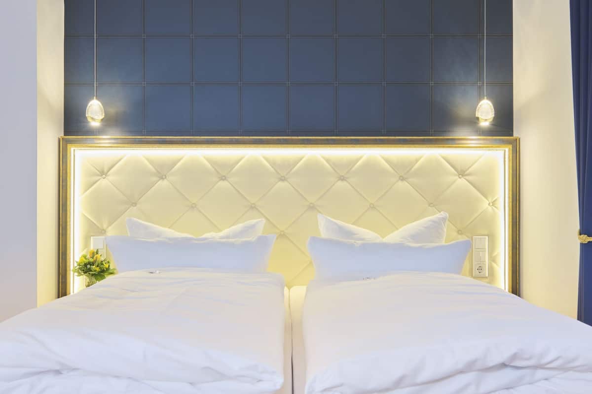 A double bed with a tufted headboard, white bedding, and a wall-mounted light fixture.