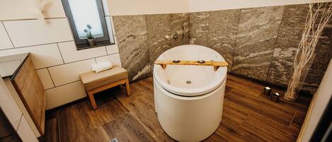 A modern bathroom with a freestanding bathtub, a wooden bench, and a window with a view.