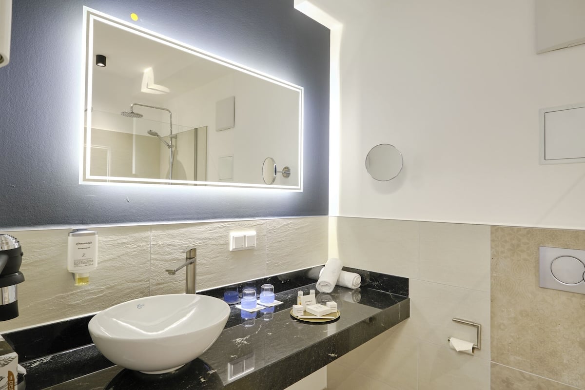 A modern bathroom with a large mirror, a white sink, and a black countertop.