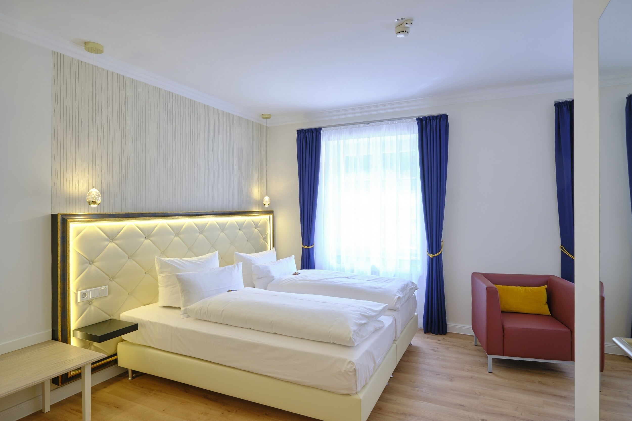 A hotel room with a large bed, bedside tables, a chair, and a window with curtains.