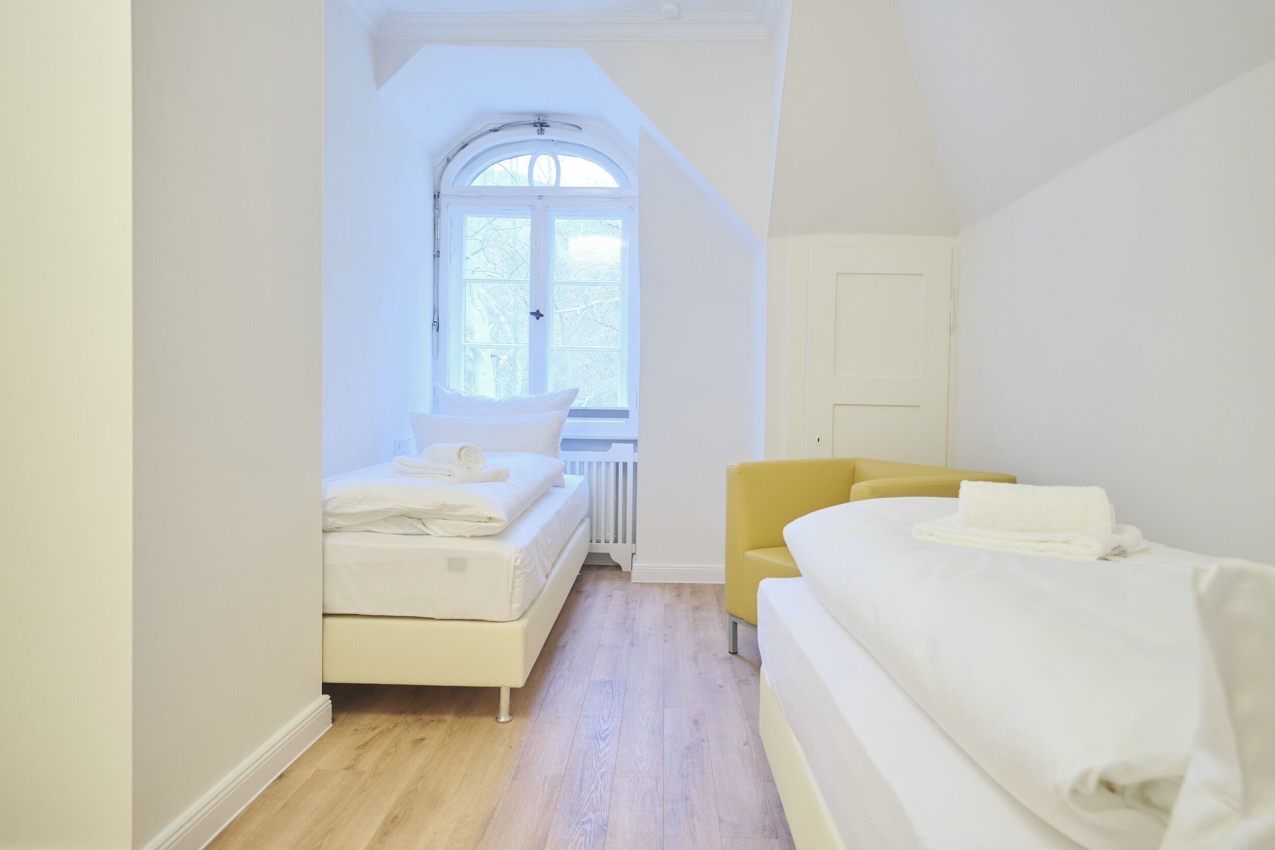 A bedroom with a white bed, a yellow chair, and a window with a view of trees.