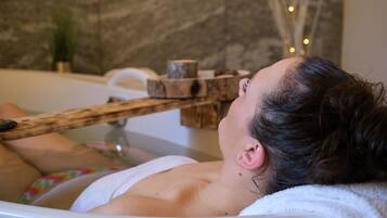 A person relaxing in a bathtub with a wooden structure above it, possibly for a spa treatment.