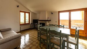 A dining area with a table and chairs, a sofa, a fireplace, and a view through a sliding door. - Bologna House (Perledo)
