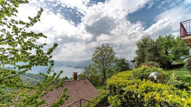 A house with a red-tiled roof, surrounded by lush greenery and a clear sky. - Bologna House (Perledo)