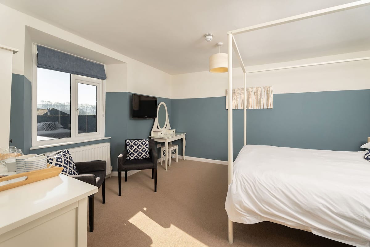 Une chambre à coucher avec un lit à baldaquin, un bureau avec une chaise, une télévision et une fenêtre donnant sur un beau paysage.