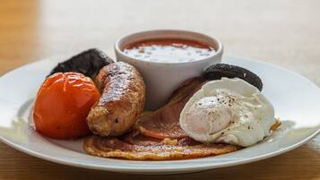 Un plato con una salchicha, un huevo pochado, tocino y tomate.