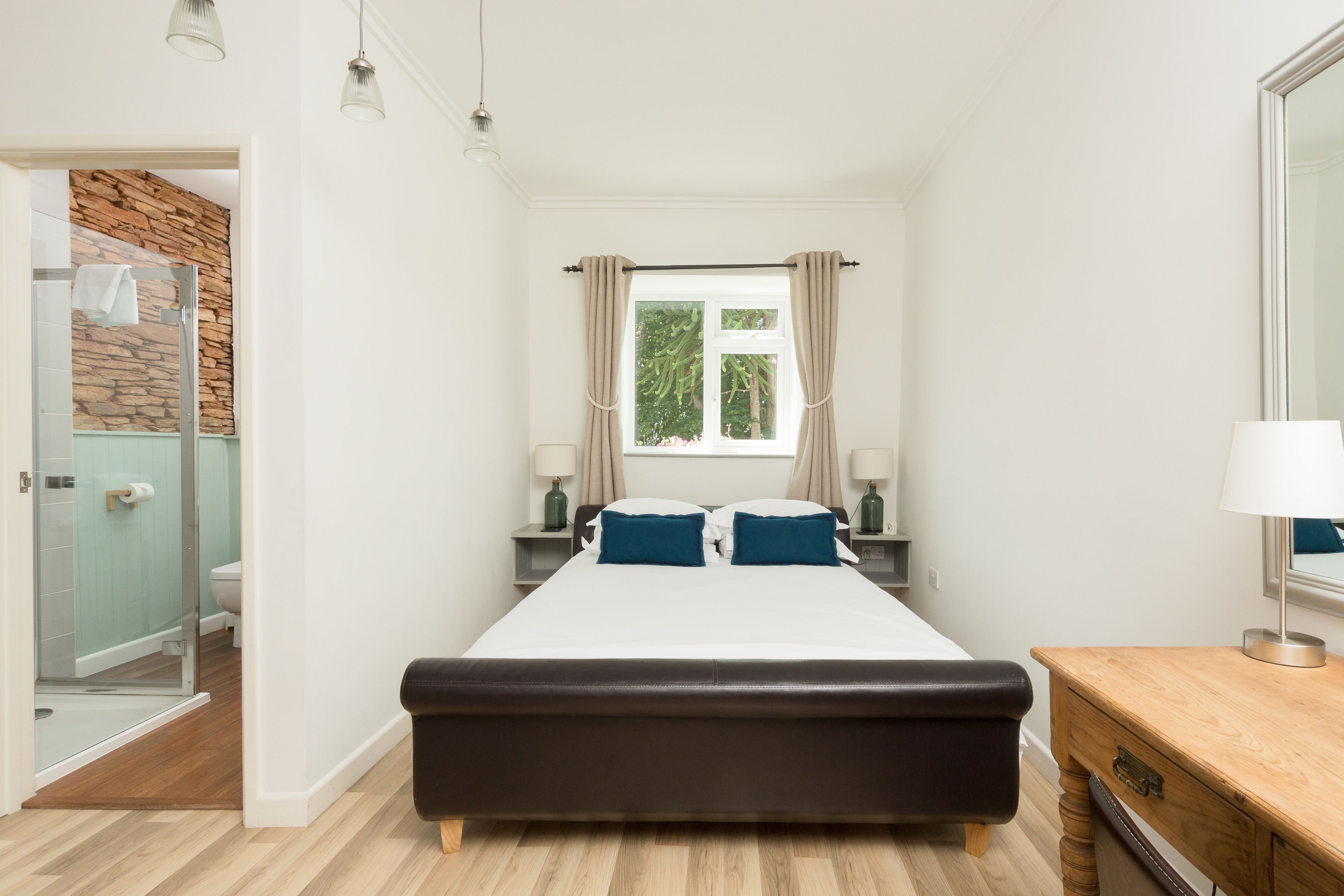 Ein modernes Schlafzimmer mit einem großen Bett, einem Nachttisch aus Holz, einem Beistelltisch, einem Spiegel und einem Fenster mit Vorhängen.