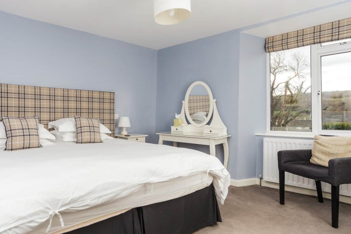 Une chambre à coucher avec un grand lit, deux tables de chevet, une commode, une chaise et une fenêtre donnant sur un beau paysage.
