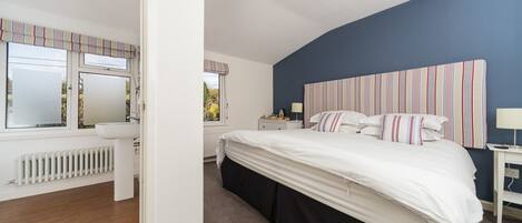 A bedroom with a large bed, a nightstand, a lamp, and a window with curtains.