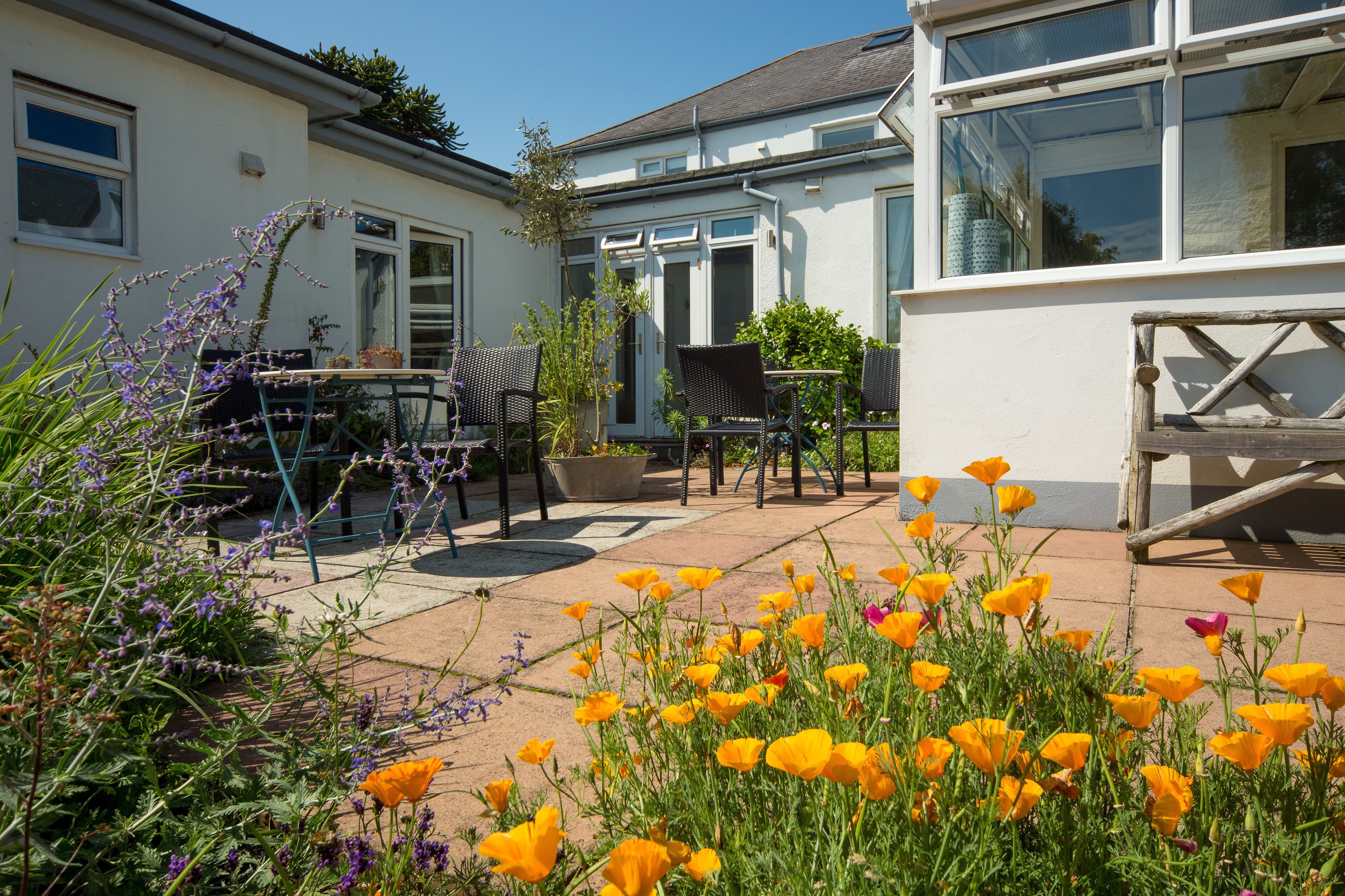 A patio with outdoor seating, a garden with poppies, and a house with large windows and a white exterior.