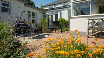 A patio with outdoor seating, a garden with poppies, and a house with large windows and a white exterior.