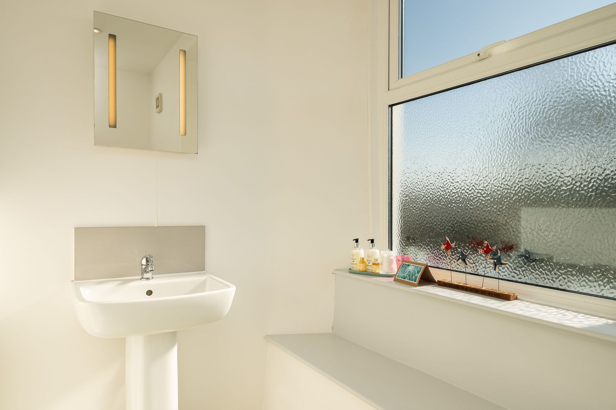 Een badkamer met een wit wastafelmeubel, een spiegel en een raam met gezandstraalde glas.