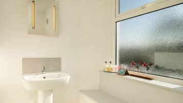 Een badkamer met een wit wastafelmeubel, een spiegel en een raam met gezandstraalde glas.