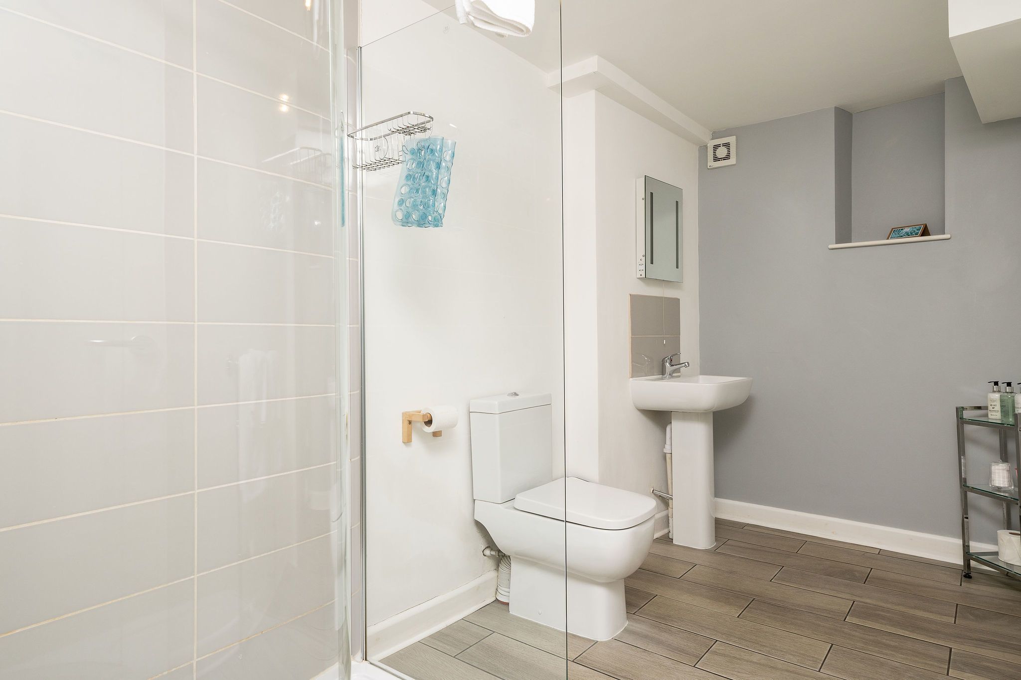 A modern bathroom with a glass shower enclosure, a toilet, a sink, and a small shelf with toiletries.