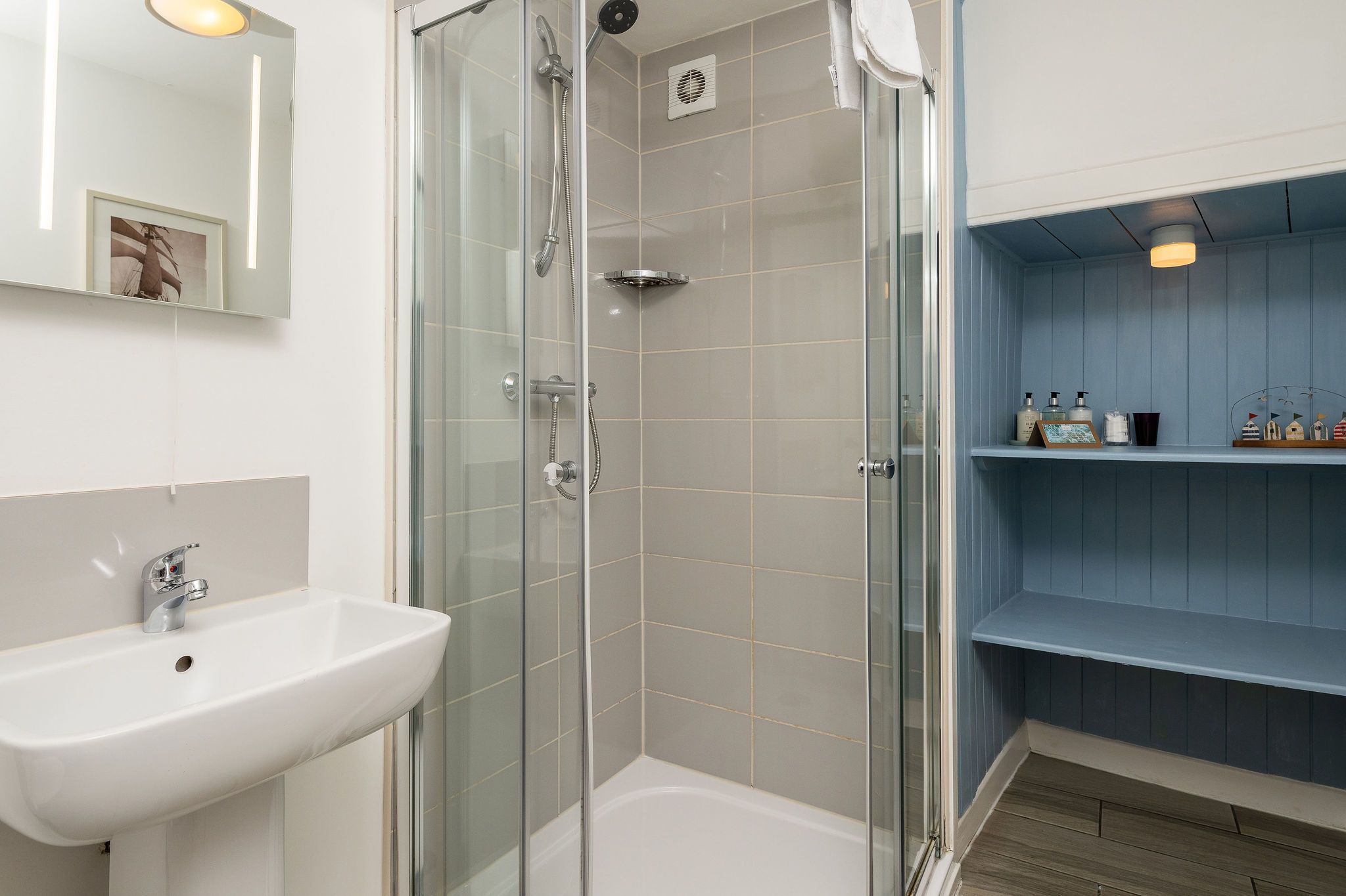A modern bathroom with a glass-enclosed shower, a white sink, and a blue vanity with shelves.