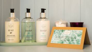 Tres productos de The Scottish Fine Soaps Company: jabón líquido para manos AU Lait Cream, champú y acondicionador de Algas Marinas, junto con una tarjeta y una vela.