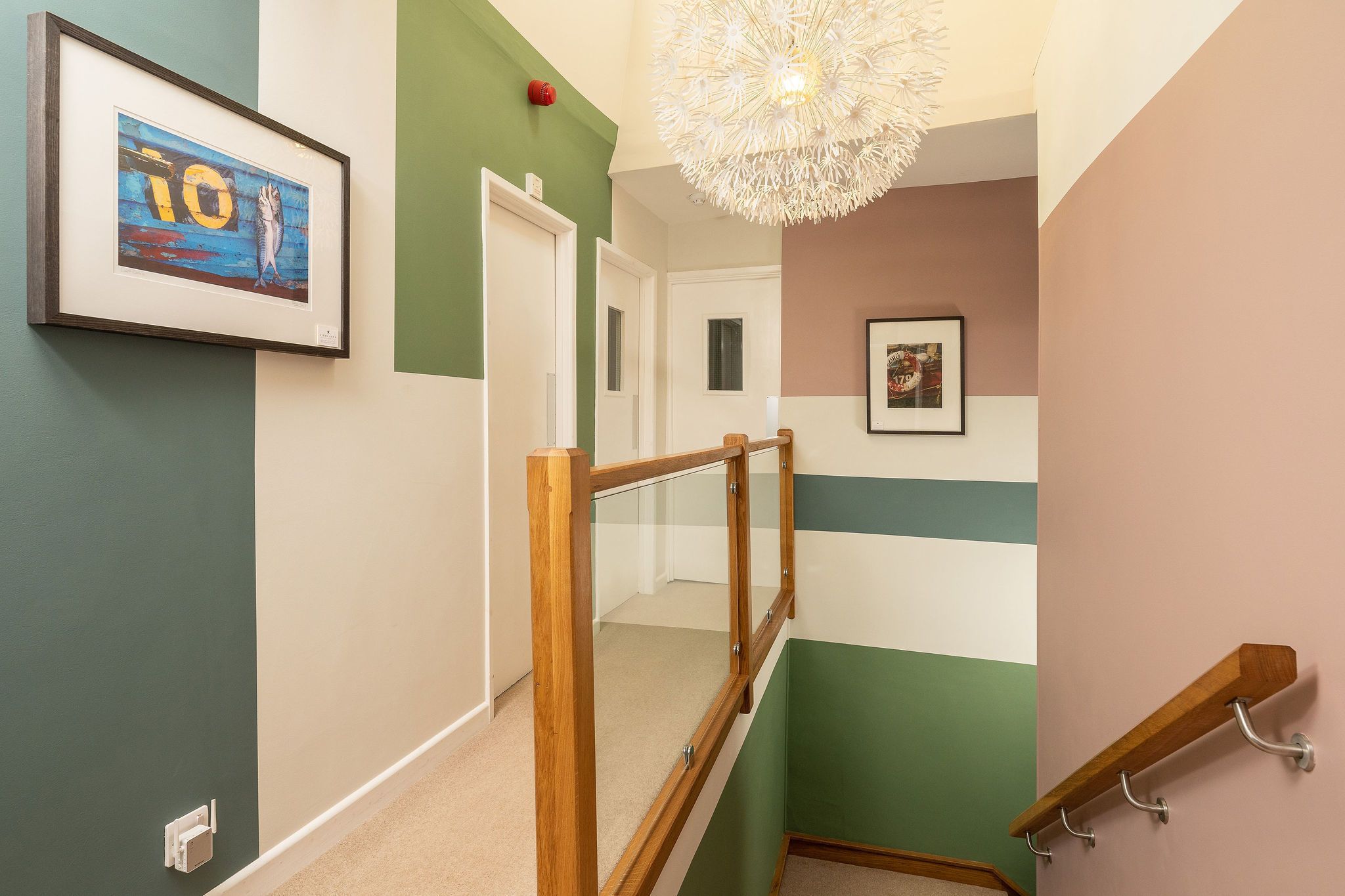 A multi-colored hallway with a wooden handrail, a framed artwork, and a ceiling light fixture.