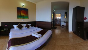 A hotel room with a large bed, a painting of a sunset, a desk with a phone, and a view into the bathroom. - Kasang Regency Hill Resort (Lansdowne)