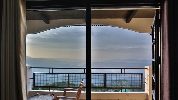 A balcony with a view of the sea and mountains, a chair, and a small table. - Kasang Regency Hill Resort (Lansdowne)