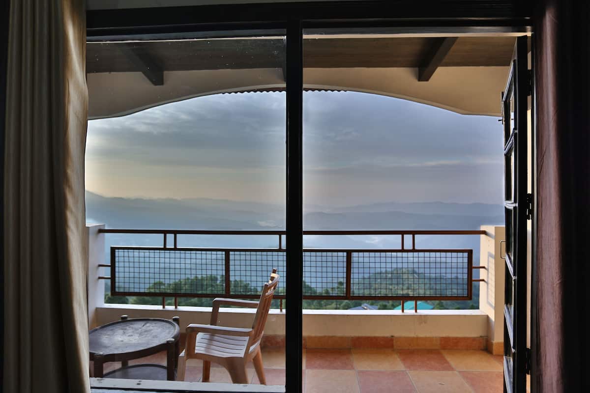 A balcony with a view of the sea and mountains, a chair, and a small table.